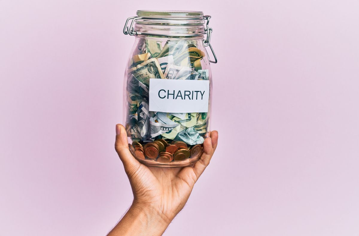 hand-man-holding-charity-jar-with-dollars-isolated-pink-background