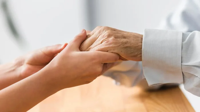 Two people holding hands, one shown as elderly 