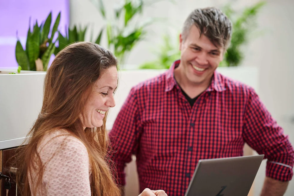 Laura Pinkstone holding a laptop and speaking with Dan Chadney who is looking at the laptop
