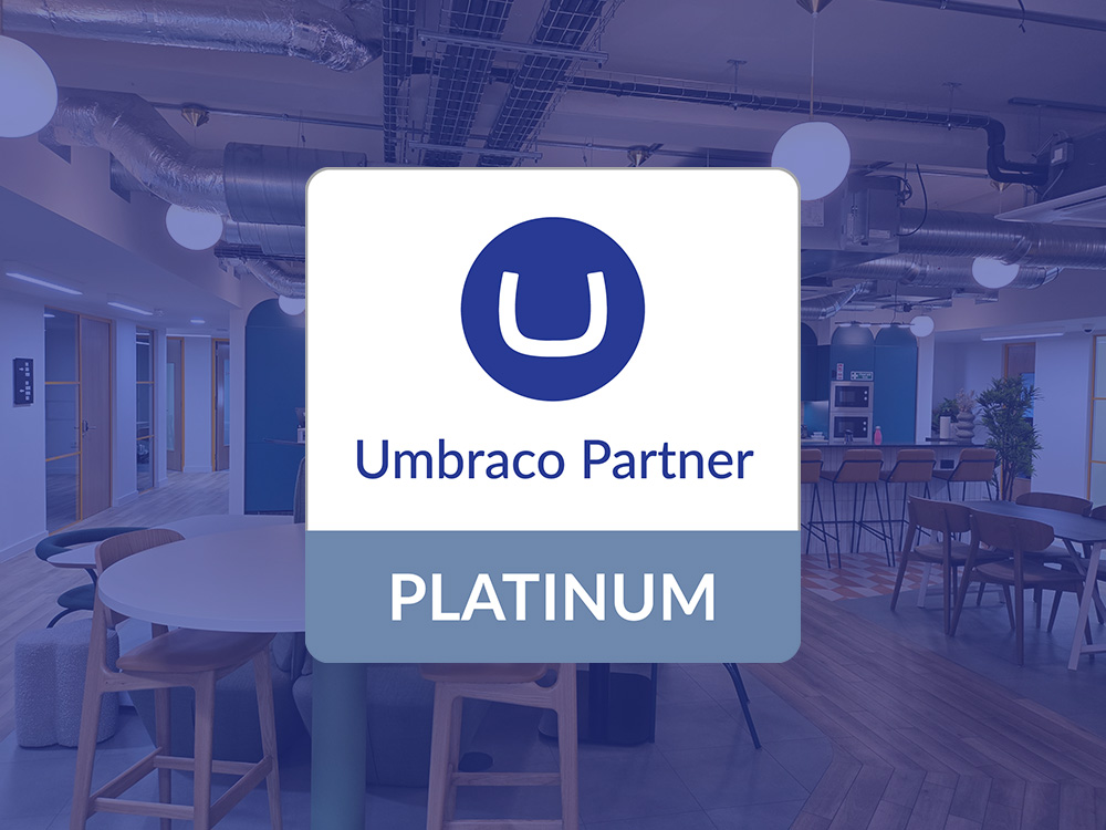 Umbraco Partner Platinum certification badge displayed in a modern office environment, featuring a blue circle with a white "U" logo and "PLATINUM" designation on a light background.